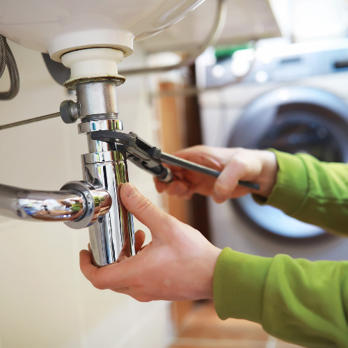 A close up of a wrench turning a pipe underneath a sink 