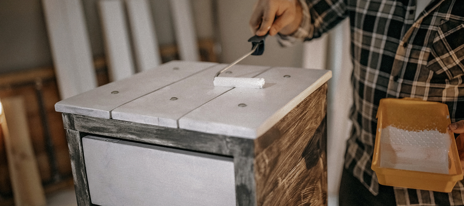 An individual using a paint roller with white paint on a night stand